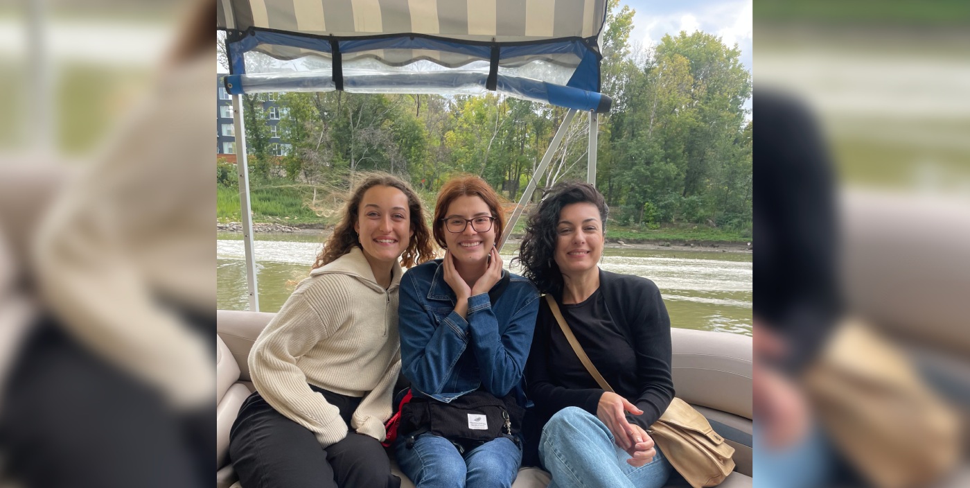 Three students smile at the camera while sitting on a pontoon boat.