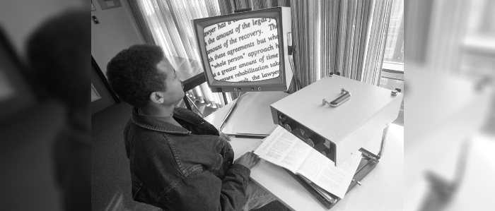 Black and white photo of student using microfilm in library
