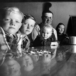 Black and white photo of three children at a table with two adults