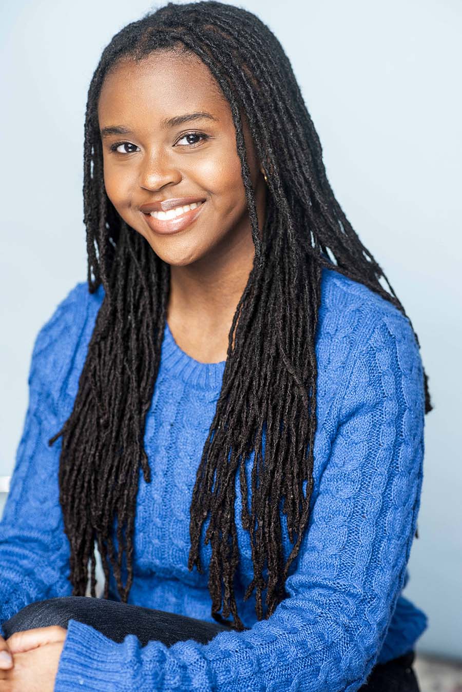 Image of a smiling black woman with long braids, wearing a bright blue sweater.
