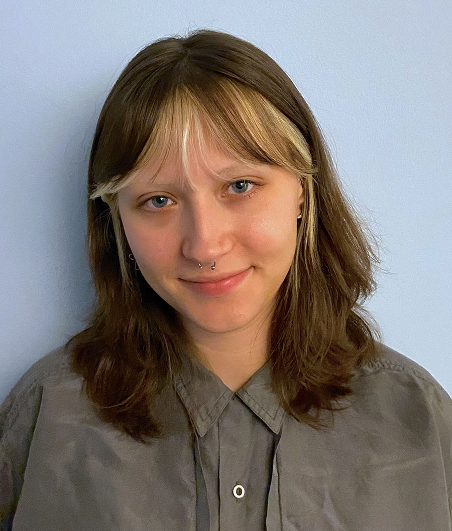 A white woman with brown hair and blonde bangs, wearing a dark grey shirt.