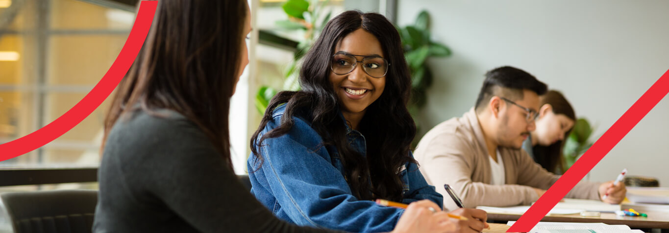 Two students in a classroom talking, two more students in the background