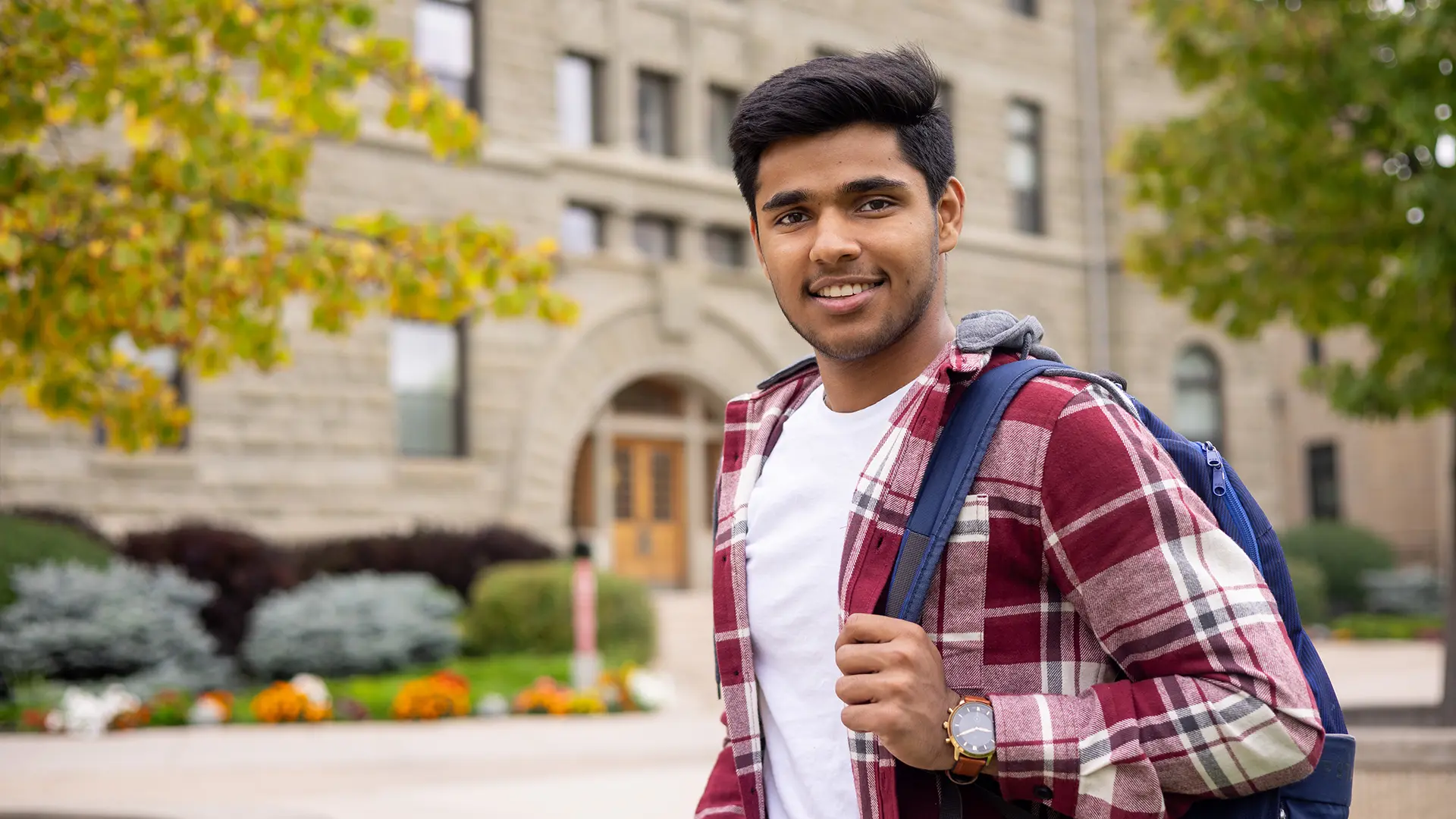Student standing in front of Wesley Hall, backpack on shoulder, smiling at camera
