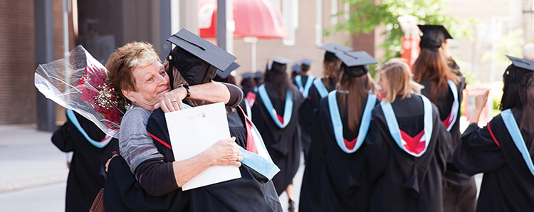 Woman hugging student at convocation, students in regalia