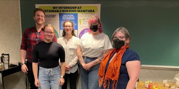 A professor and four students standing by a table in front of a chalkboard.