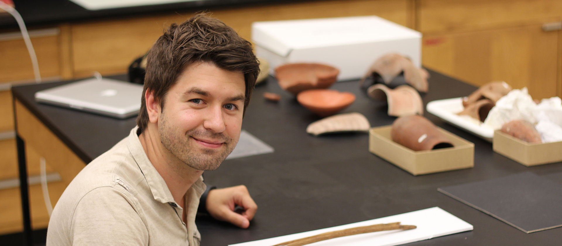 Student in a classroom, looking up at camera, artifacts on the desk.