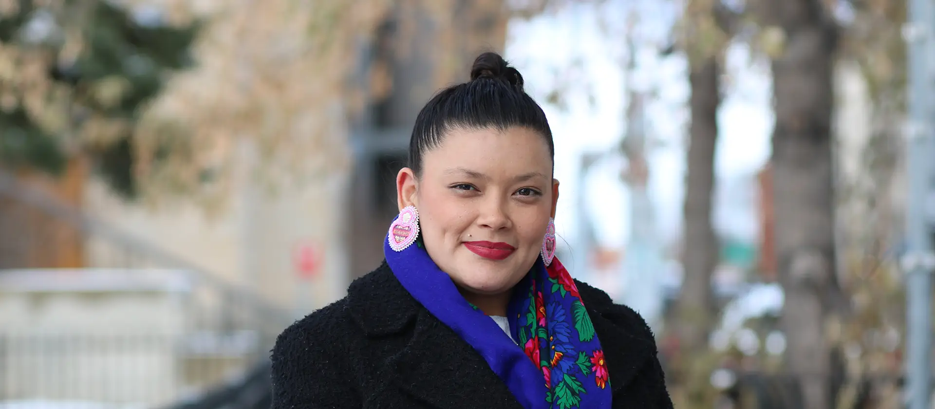 Woman in a black coat with colourful scarf and earrings smiling at the camera