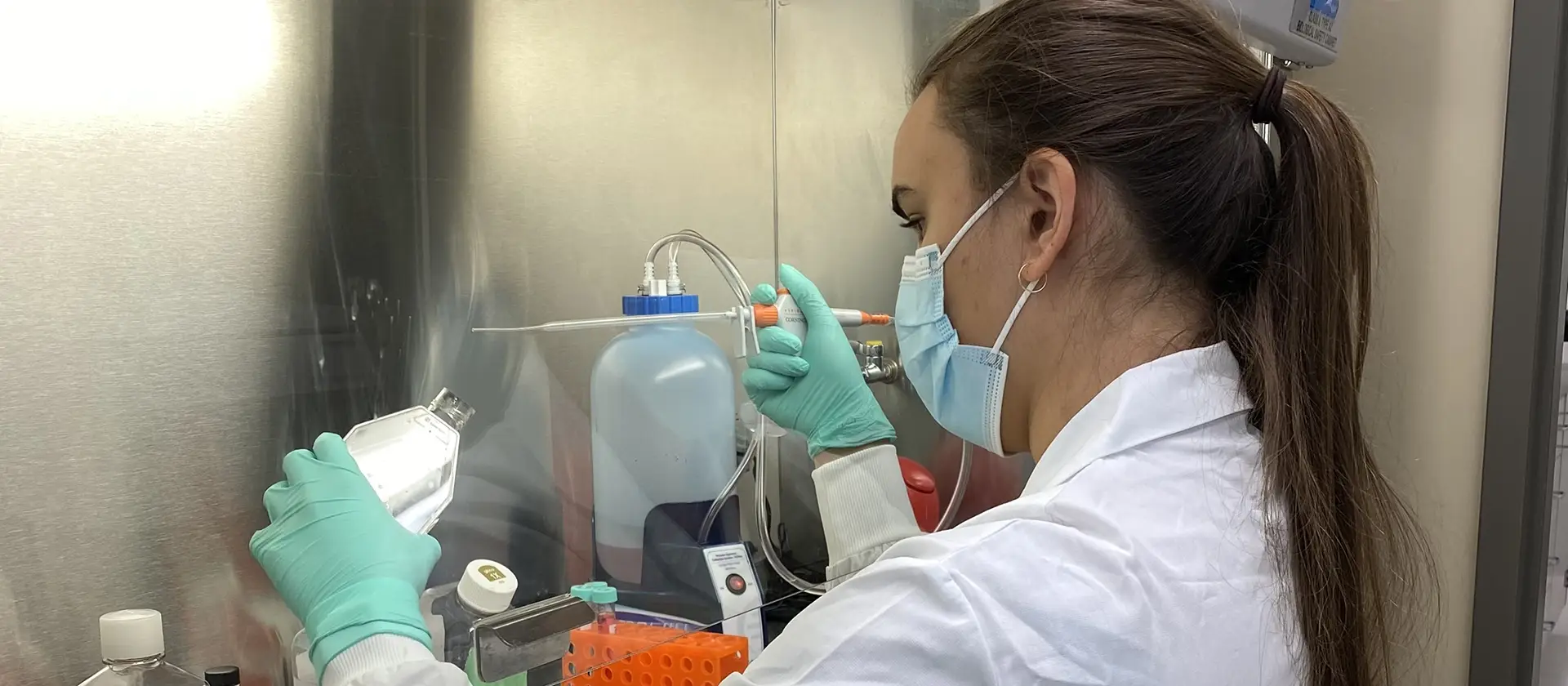 Student in a lab working with samples wearing labcoat, mask and gloves