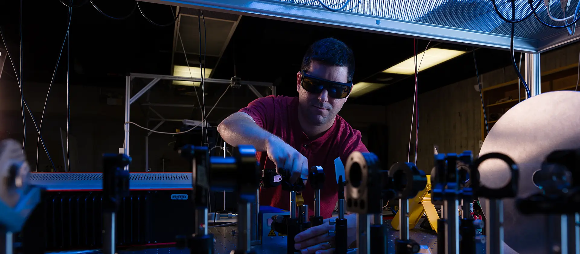 Man wearing sunglasses in dark physics lab using instruments