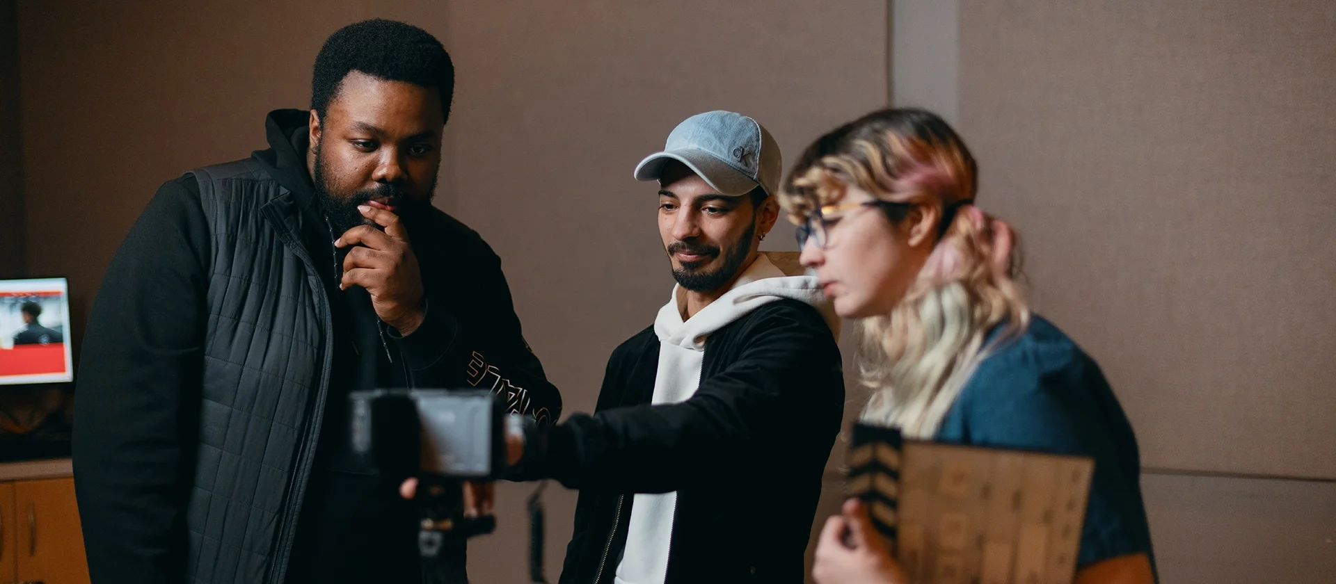Three students looking at the viewfinder of a camera