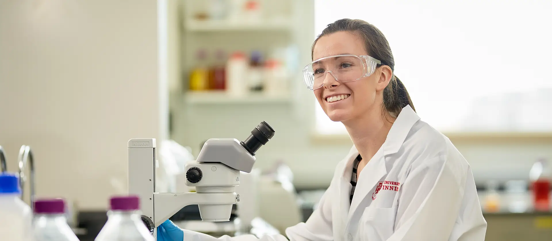 Student in a lab coat with a microscope smiling