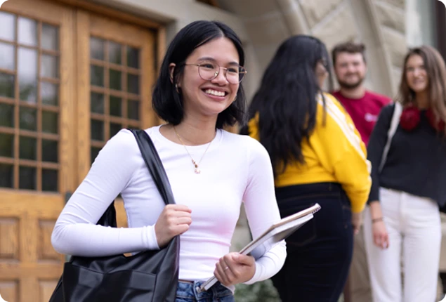 Student standing on front steps holding books and smiling
