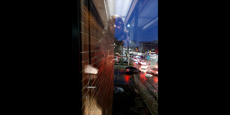 Reflection of a woman in a window looking at a busy city street with cars at night