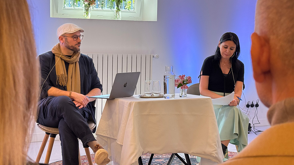 A man and woman are sitting at a table wearing small headsets.