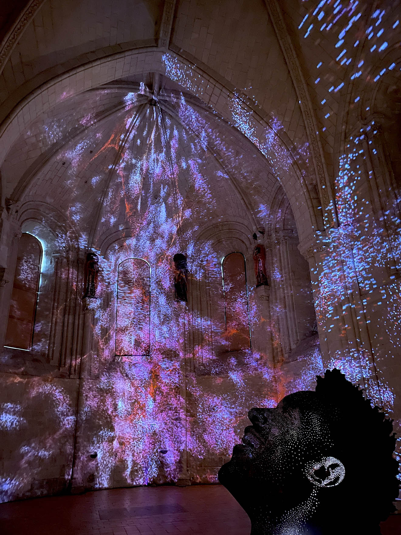 Dark cathedral with purple, red and blue lights shining n the walls and ceiling, outline of a person looking up and smiling