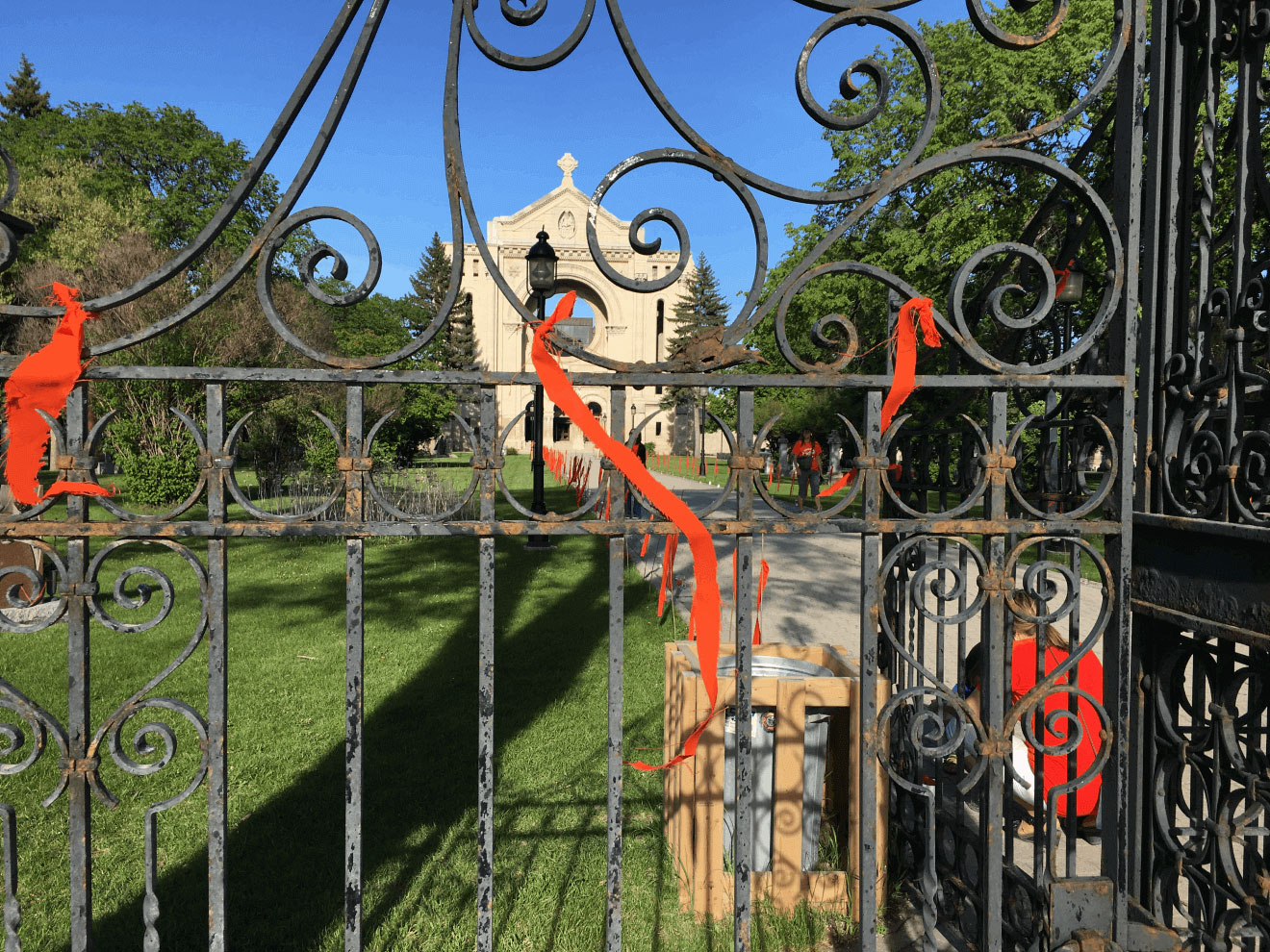 Orange ribbons on a wrought iron gate. Green grass and tall stone building in the background.