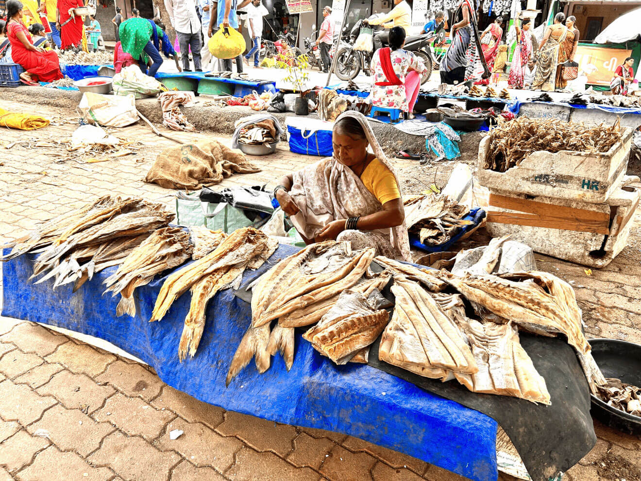 A woman sitting on the ground in a market behind a table full of fish.