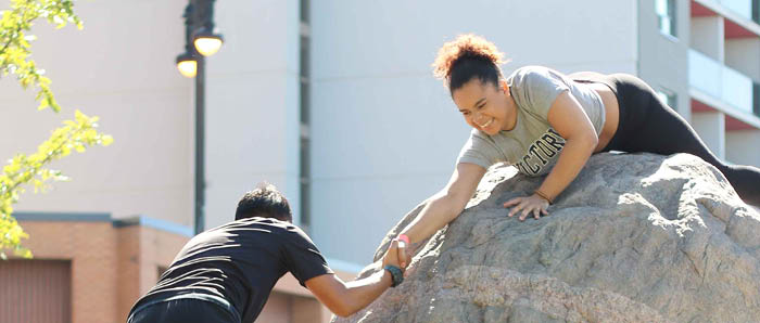 Person at top of the rock helping second person ip