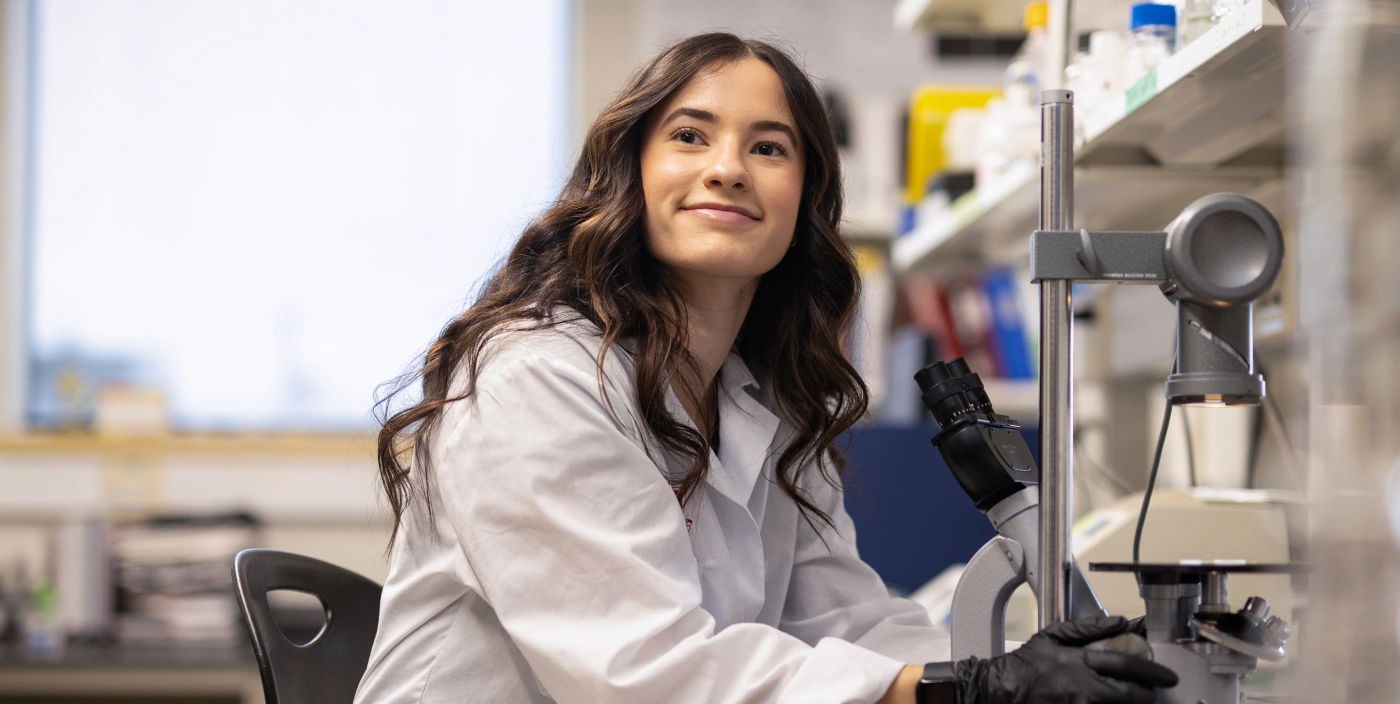 Student Hailey Langford in a lab coat using a microscope