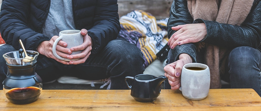 Two people on a couch with coffee and tea.  