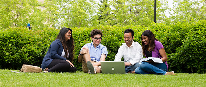 Four UWinnipeg Students on front lawn looking at laptop