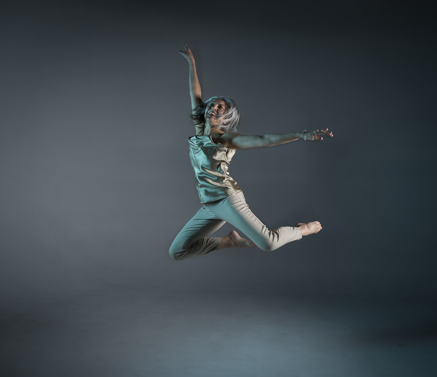 Brenda is shown leaping into the air wearing tan coloured pants and a cgolden coloured camisole. Her hair is flying and her expression is exuberant.