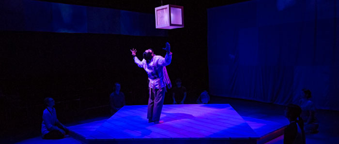  A man stands on a raised platform in a gesture of worship to a glowing box suspended above him