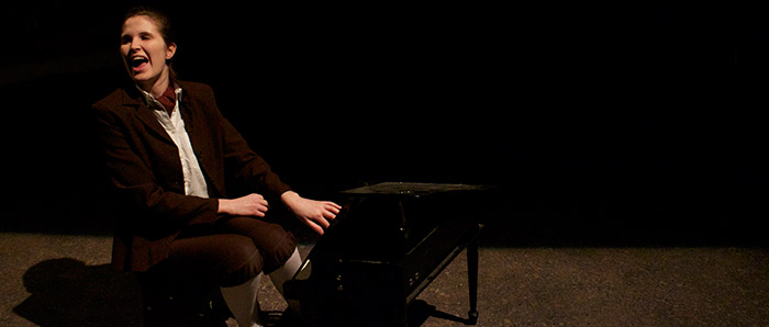 A woman in a school boy uniform playing a tiny piano