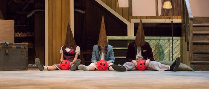Three coneheaded figures sit dejectedly in a wood panelled basement holding red balls with sad faces painted on them