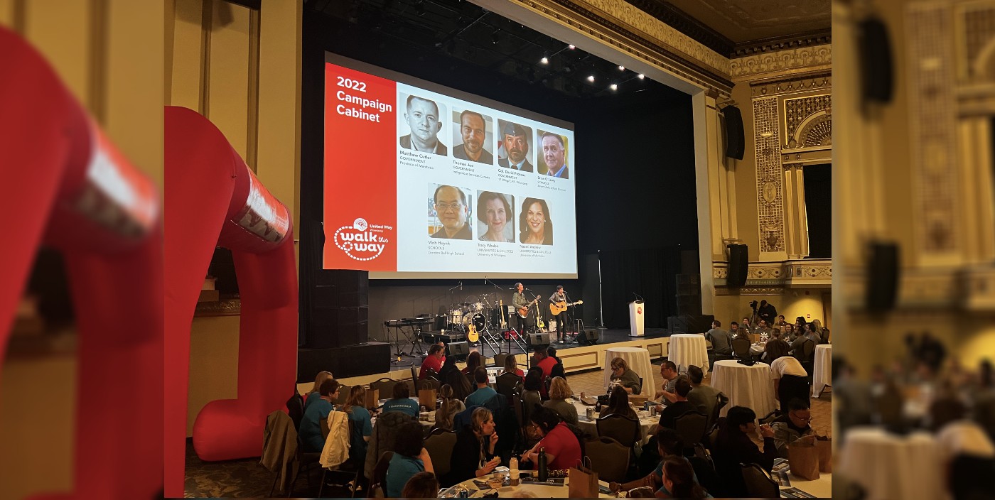 A wide photo of a large theatre venue. On stage, a band plays in front of a projection that reads '2022 Campaign Cabinet.'