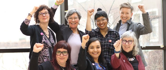 Faculty members group shot in a hall with fists raised